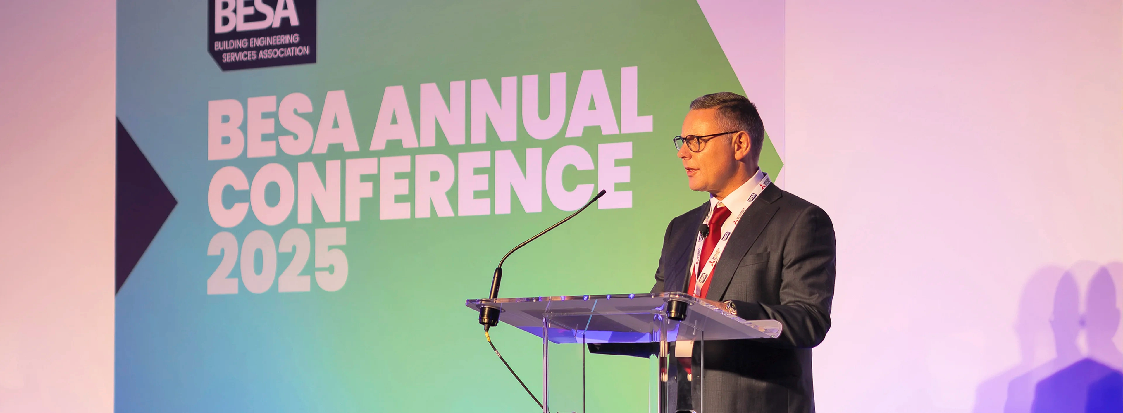 BESA Keynote speaker standing in front of BESA annual conference 2025 event designs.